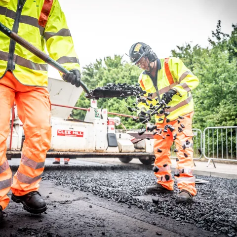 Worker shovels fresh asphalt onto new road